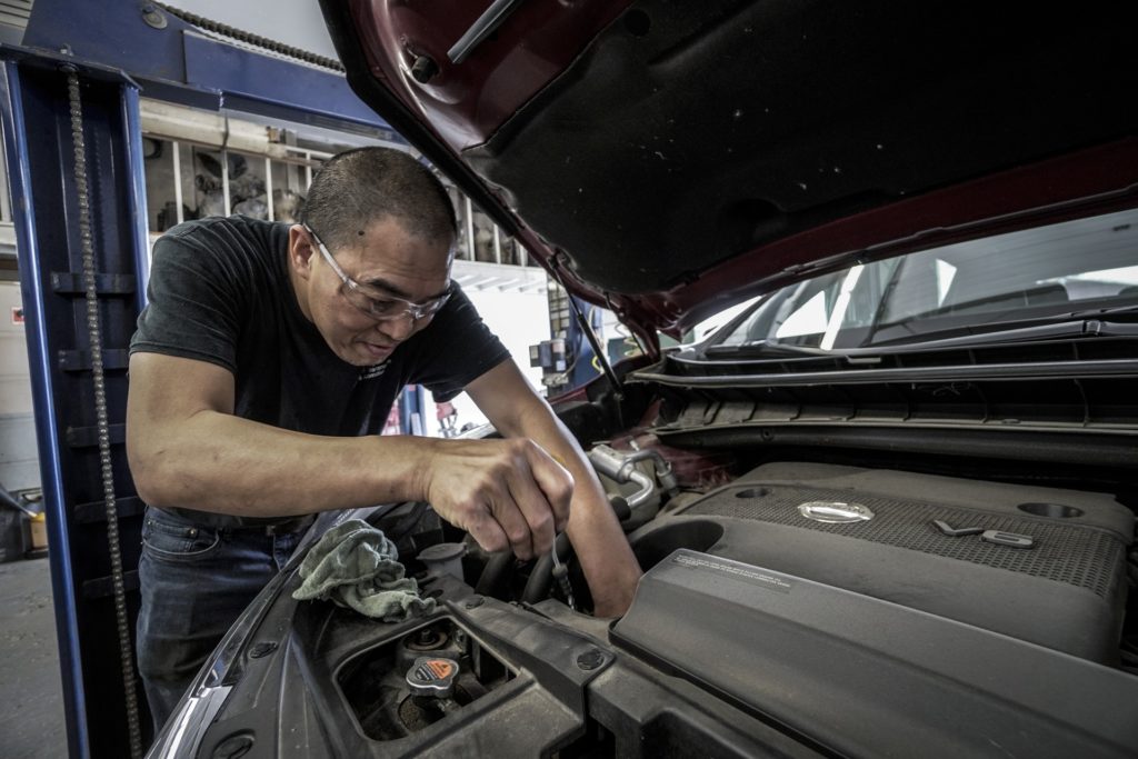 car mechanic working under the hood of a van on a V6 engine