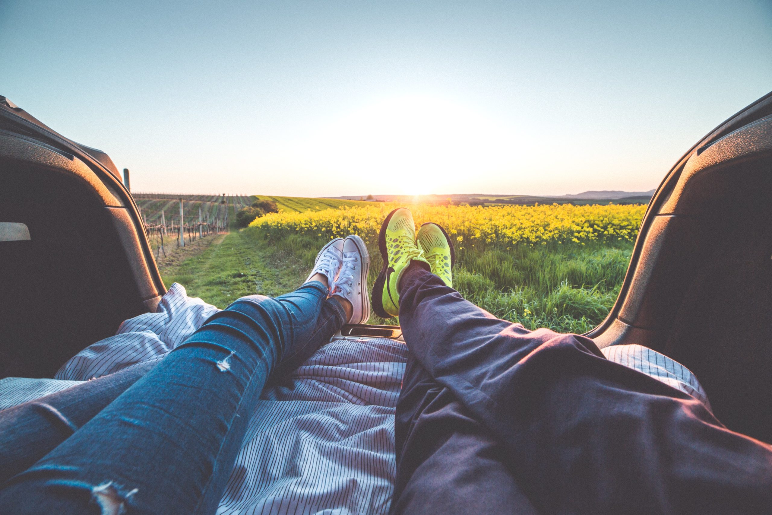 View of couple's feet as they sit in the back of a car and watch a scenic sunset over a field of flowers