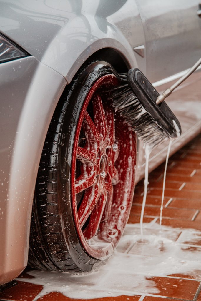 scrubbing the tire and rim of a sports car with a sudsy brush