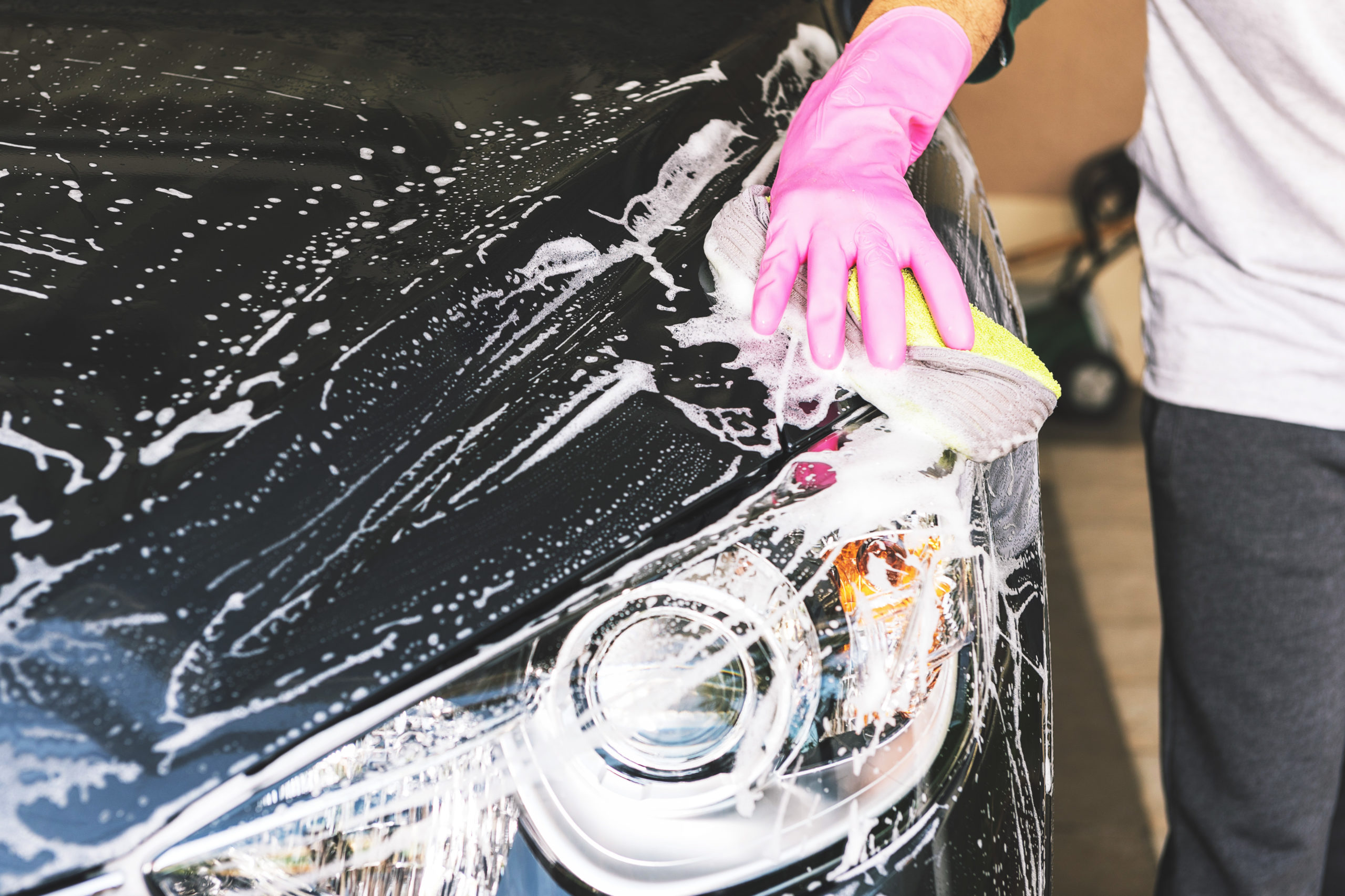 person washing black car with glove, sponge and soap