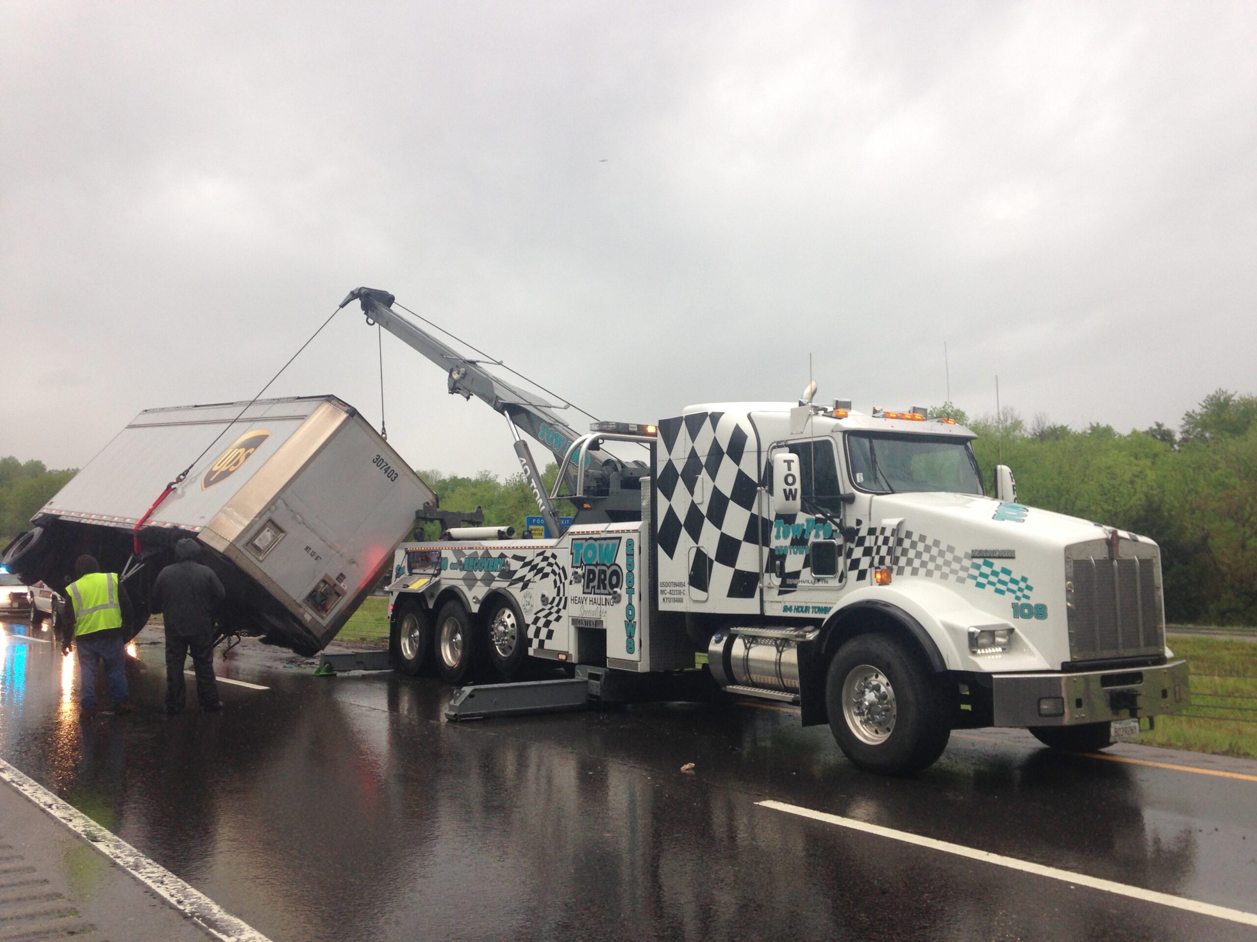 A heavy duty Tow Pro tow truck lifting up and over turned UPS truck.